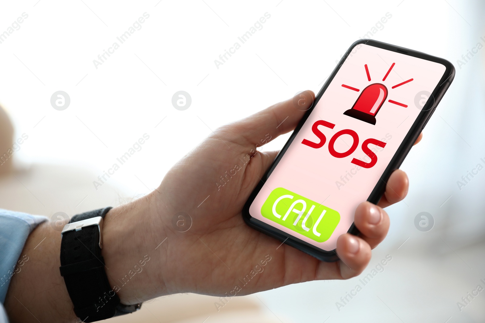 Image of Man holding smartphone with emergency call SOS on screen indoors, closeup