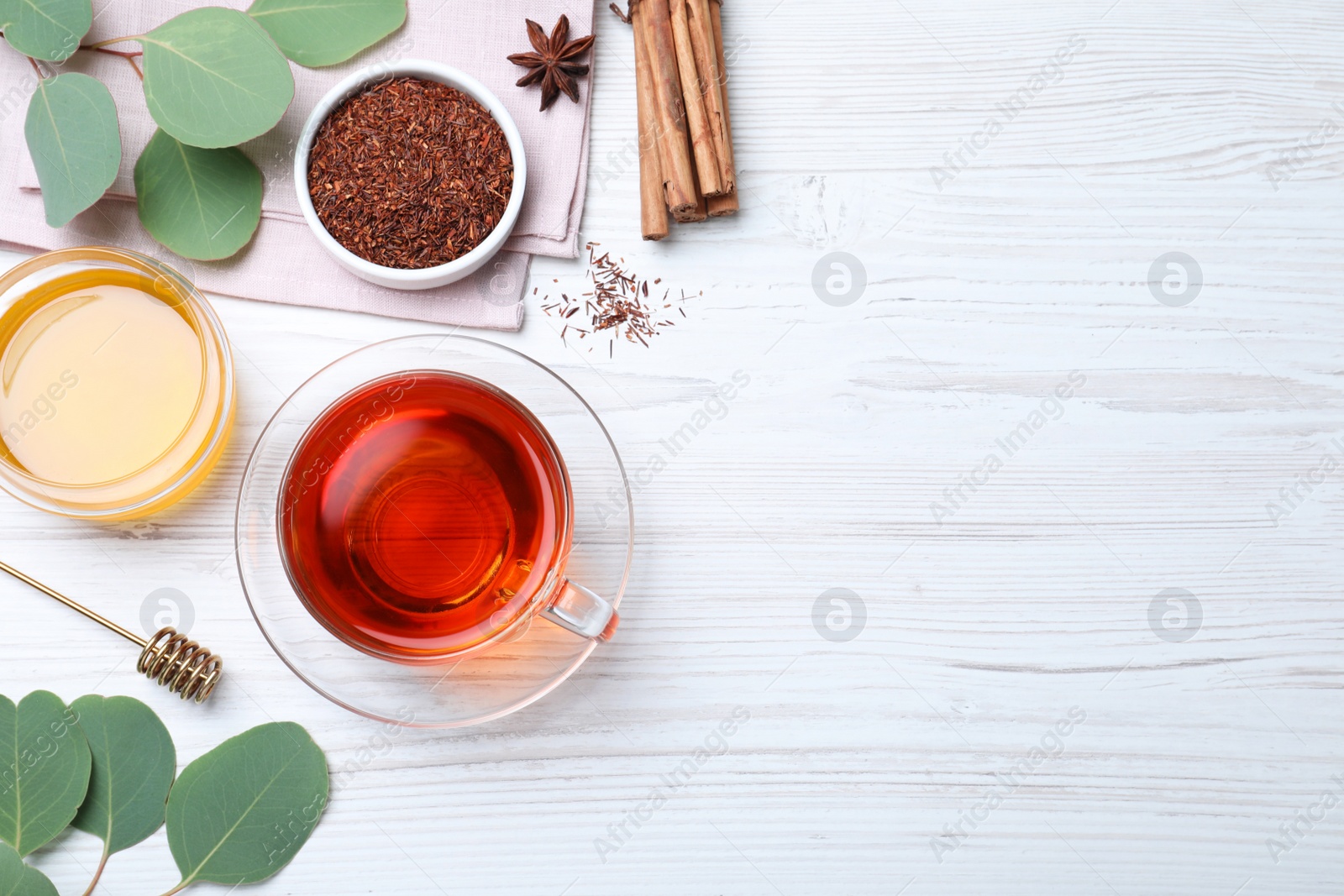 Photo of Freshly brewed rooibos tea, dry leaves, honey and spices on white wooden table, flat lay. Space for text