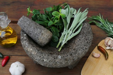 Mortar, different herbs, vegetables and oil on wooden table, closeup