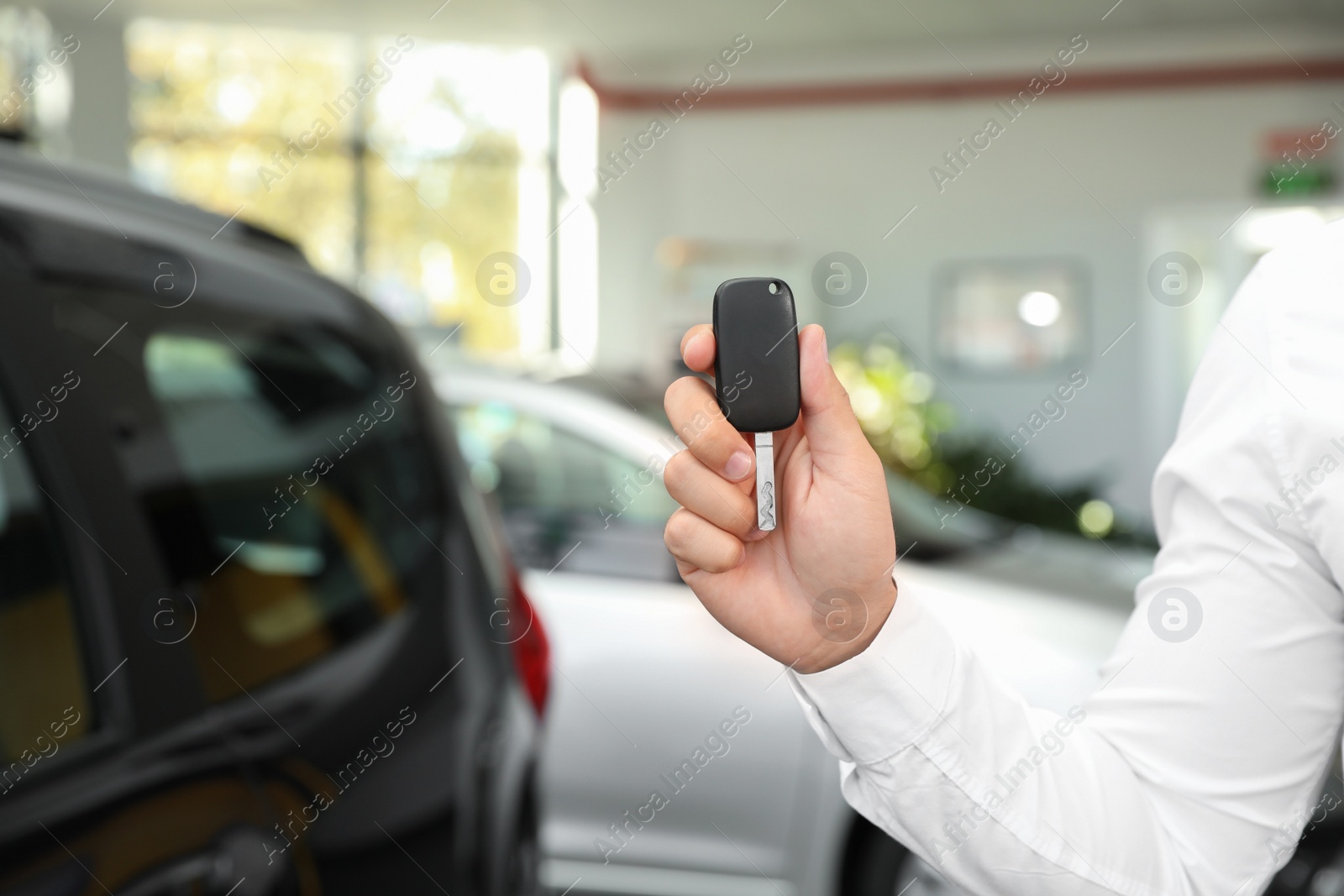 Photo of Young man with car key in dealership, closeup