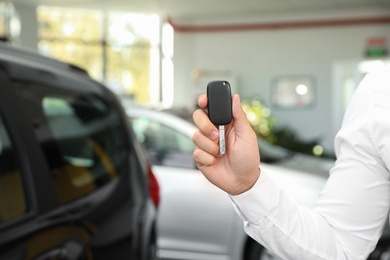 Photo of Young man with car key in dealership, closeup