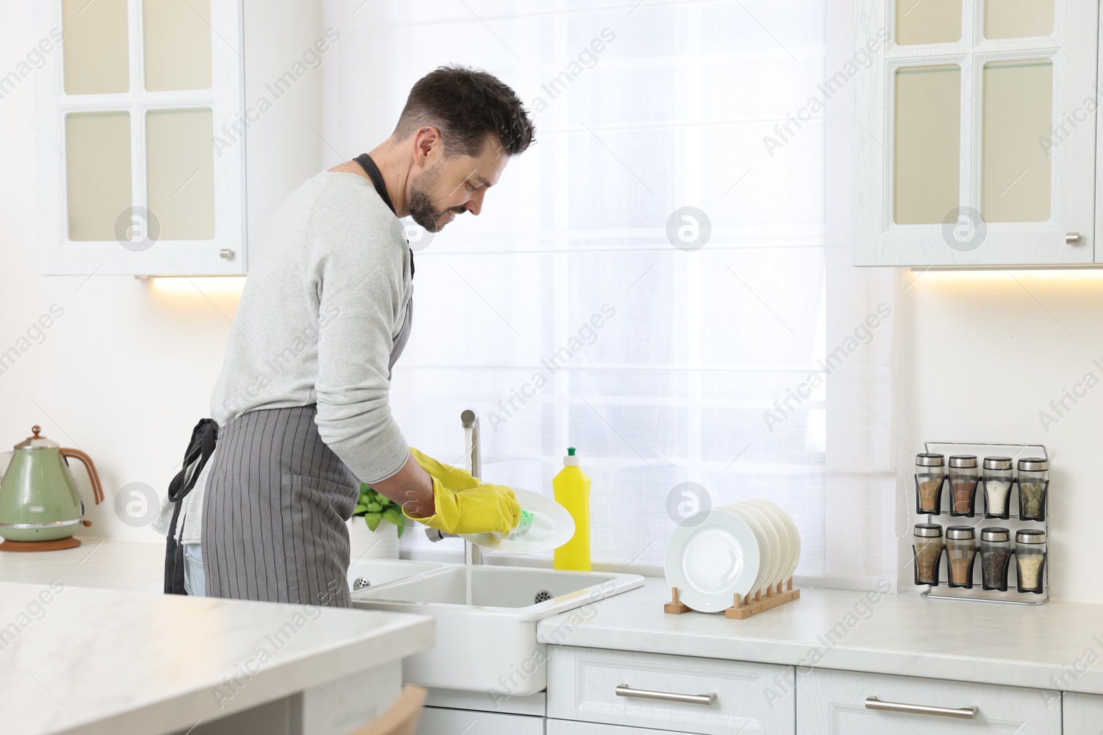 Photo of Man washing plate above sink in kitchen