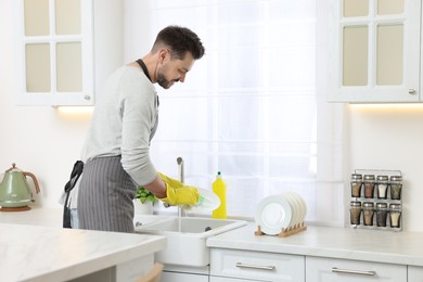 Man washing plate above sink in kitchen