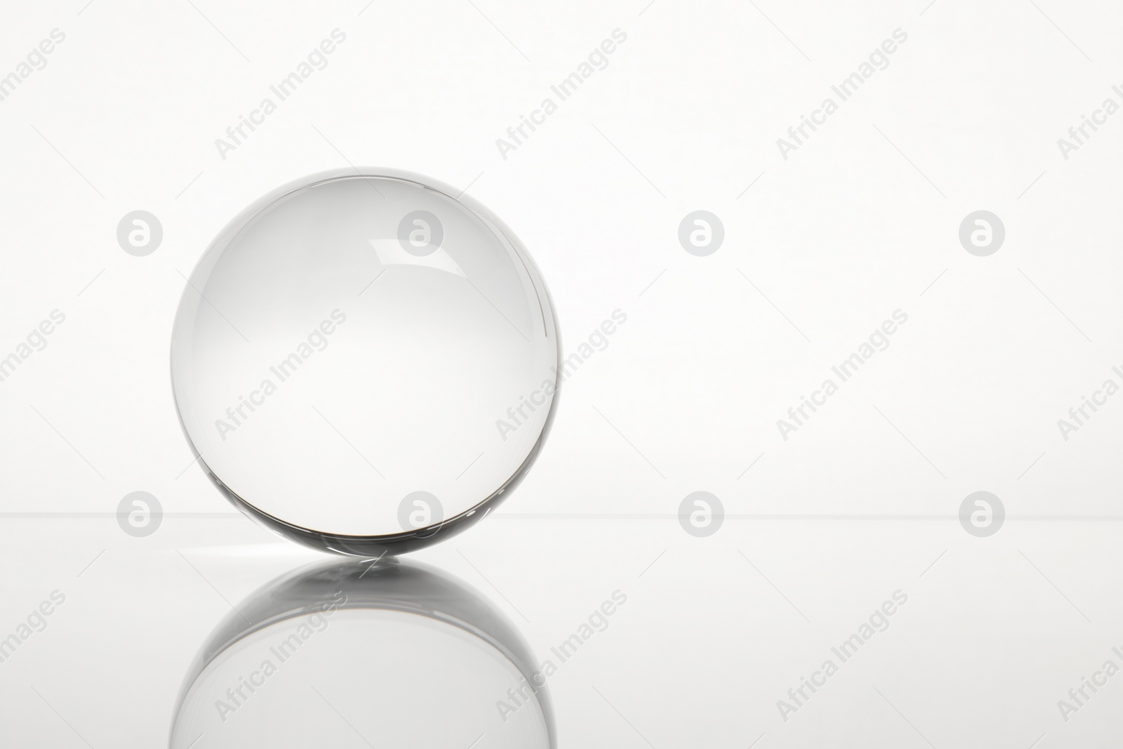 Photo of Transparent glass ball on mirror surface against white background. Space for text