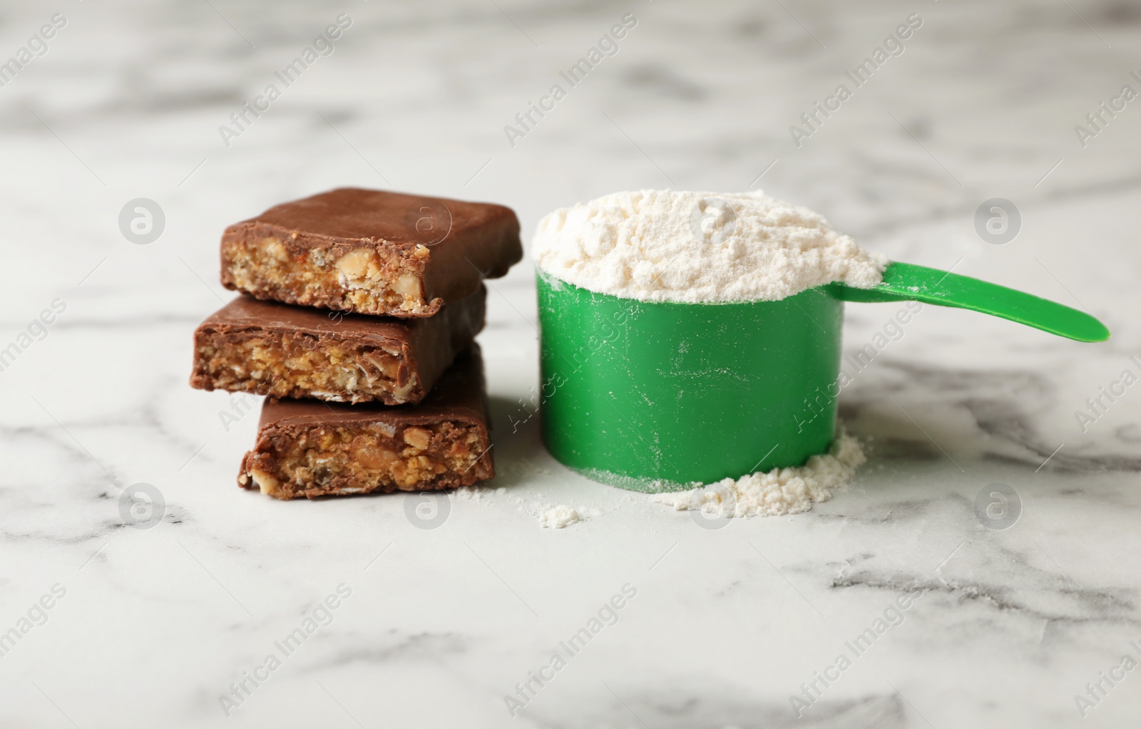 Photo of Tasty protein bar and scoop of powder on marble table