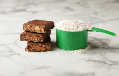 Photo of Tasty protein bar and scoop of powder on marble table