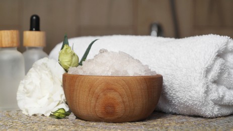 Photo of Bowl with bath salt and cosmetic product near fluffy towel on wicker mat indoors