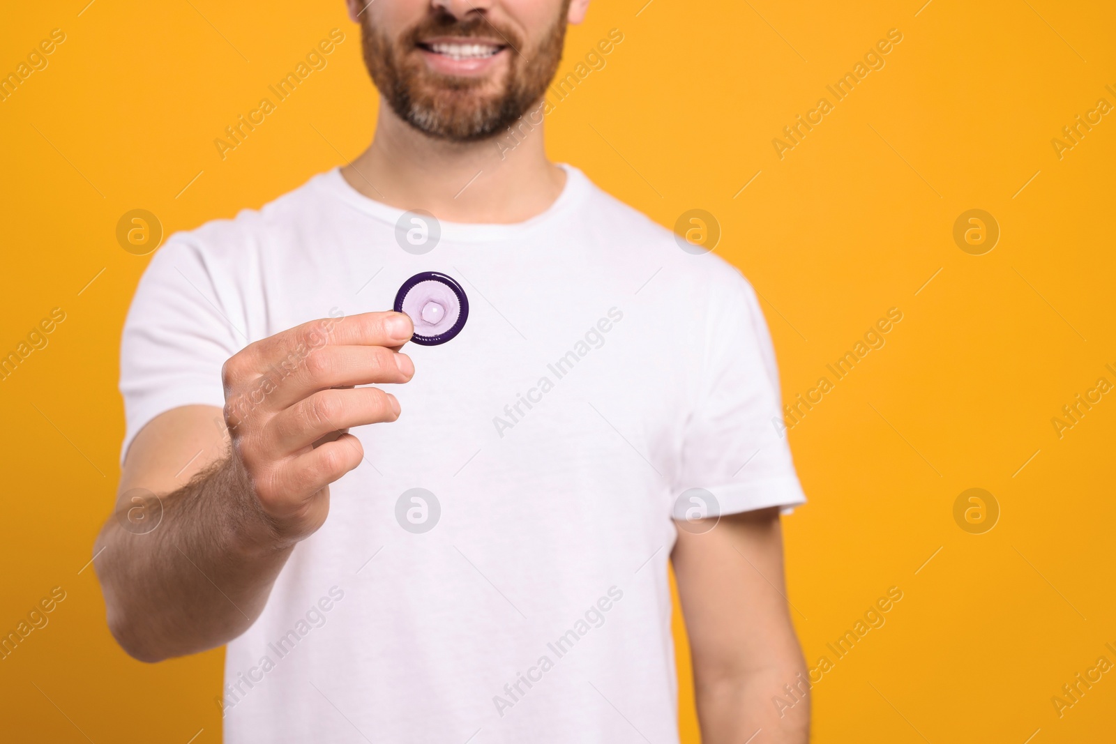 Photo of Man holding condom on yellow background, closeup. Safe sex