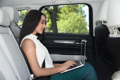 Young businesswoman with laptop in luxury car. Chauffeur service