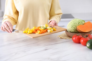Photo of Woman holding cutting board with mix of fresh vegetables in kitchen, closeup