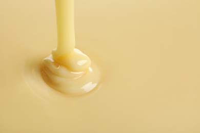 Photo of Tasty pouring condensed milk as background, space for text. Dairy product