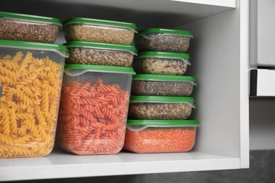 Photo of Plastic containers filled with food products in kitchen cabinet, closeup