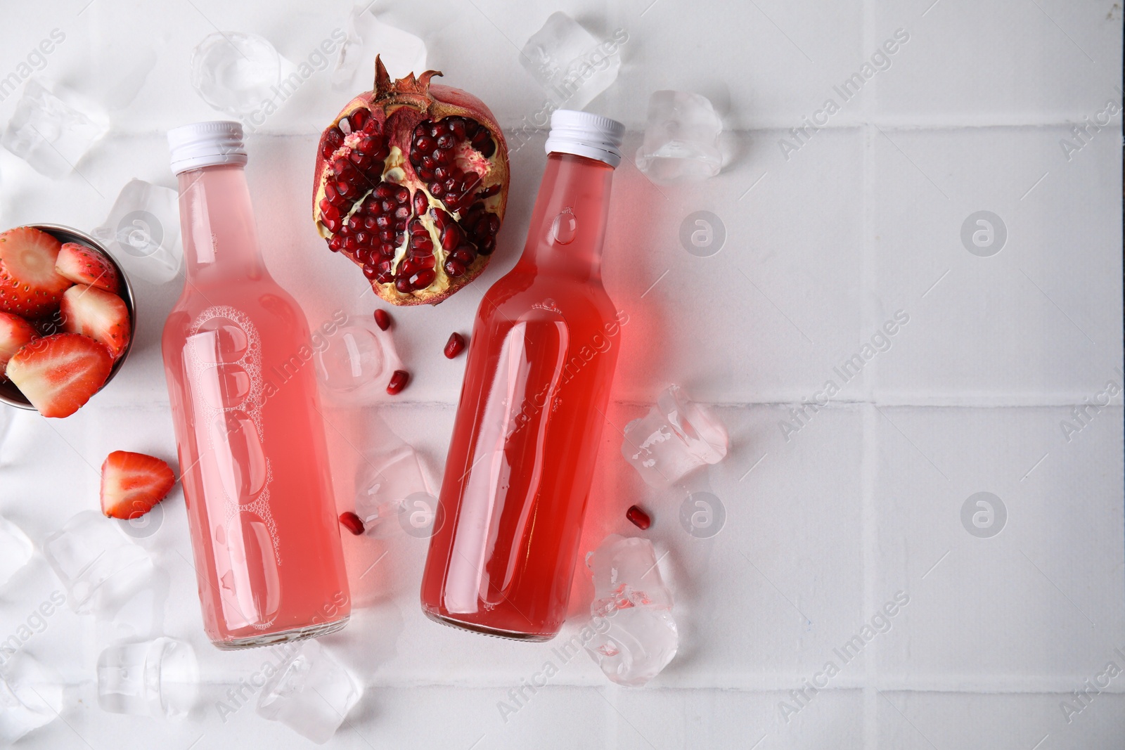 Photo of Tasty kombucha in glass bottles, fresh fruits and ice on white tiled table, flat lay. Space for text