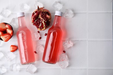 Photo of Tasty kombucha in glass bottles, fresh fruits and ice on white tiled table, flat lay. Space for text