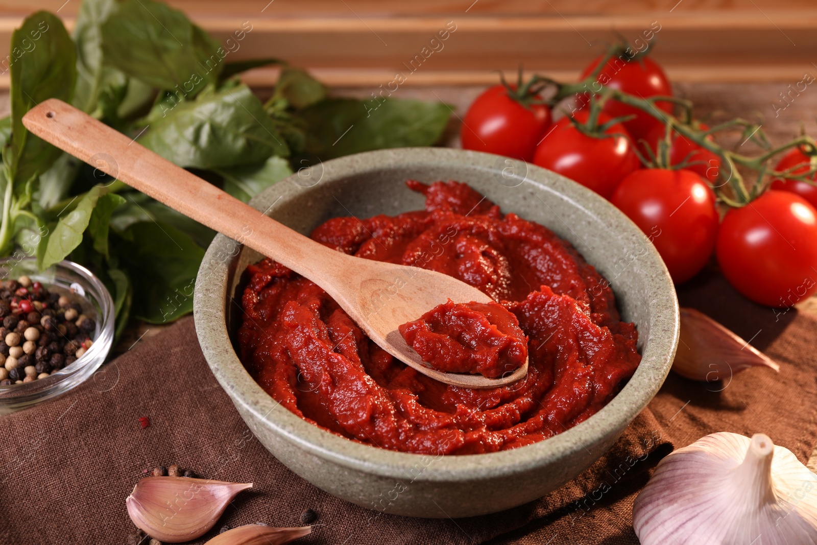 Photo of Bowl of tasty tomato paste with spoon and ingredients on table