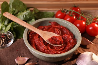 Bowl of tasty tomato paste with spoon and ingredients on table