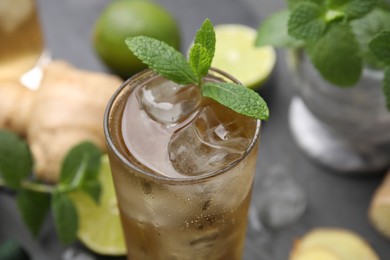Photo of Glass of tasty ginger ale with ice cubes and mint on blurred background, closeup