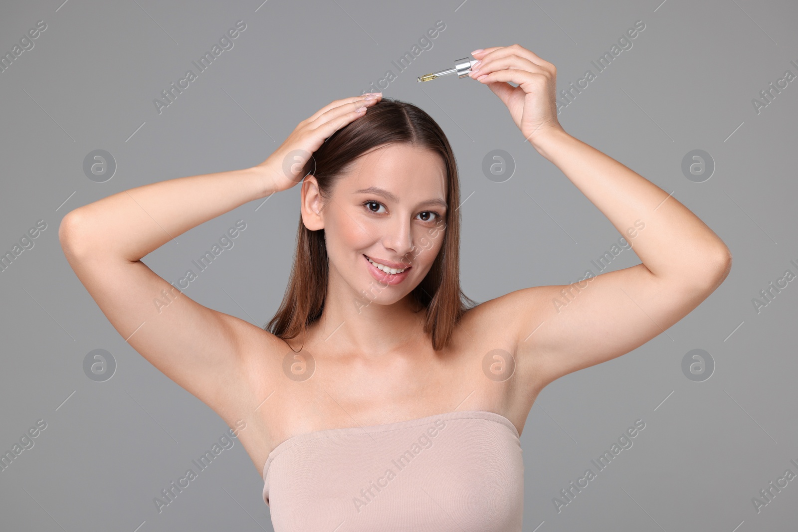Photo of Beautiful woman applying serum onto hair on grey background