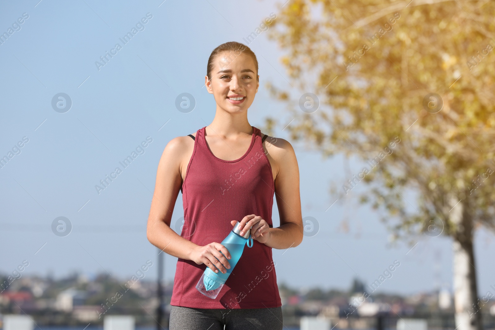 Photo of Young sporty woman holding bottle of water outdoors on sunny day