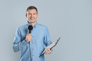 Male journalist with microphone and clipboard on grey background. Space for text