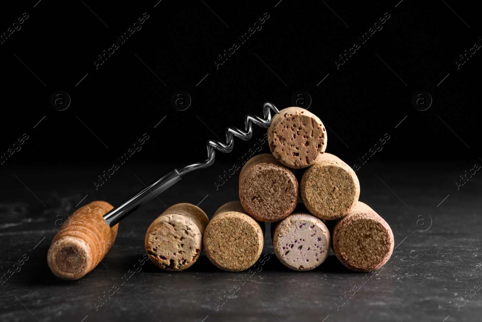 Photo of Corkscrew and stack of wine bottle stoppers on slate table, closeup