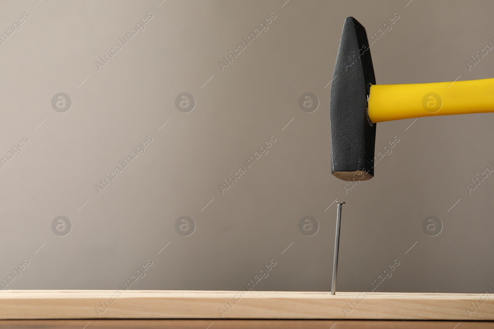 Photo of Hammering metal nail on wooden table against grey background. Space for text