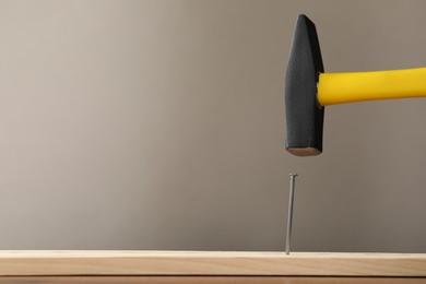 Photo of Hammering metal nail on wooden table against grey background. Space for text