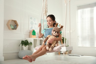 Photo of Cute little girl playing with toy deer on swing at home