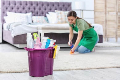 Bucket with cleaning supplies and woman in uniform on background