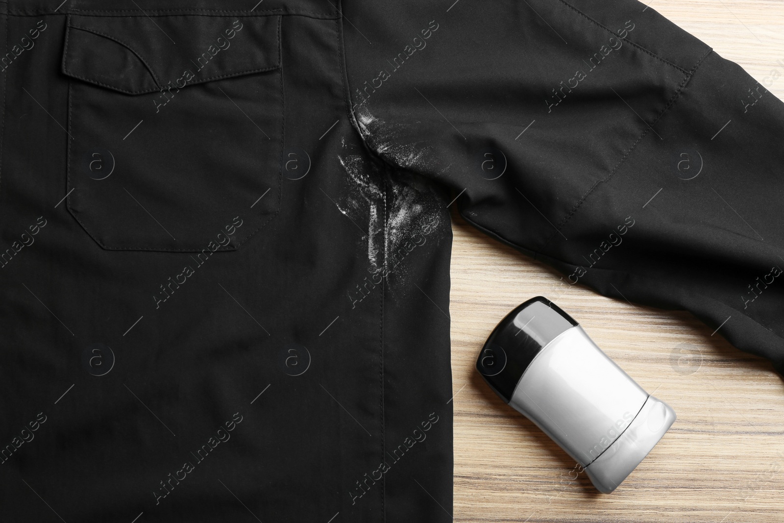 Photo of Black shirt with stain and deodorant on wooden background, top view