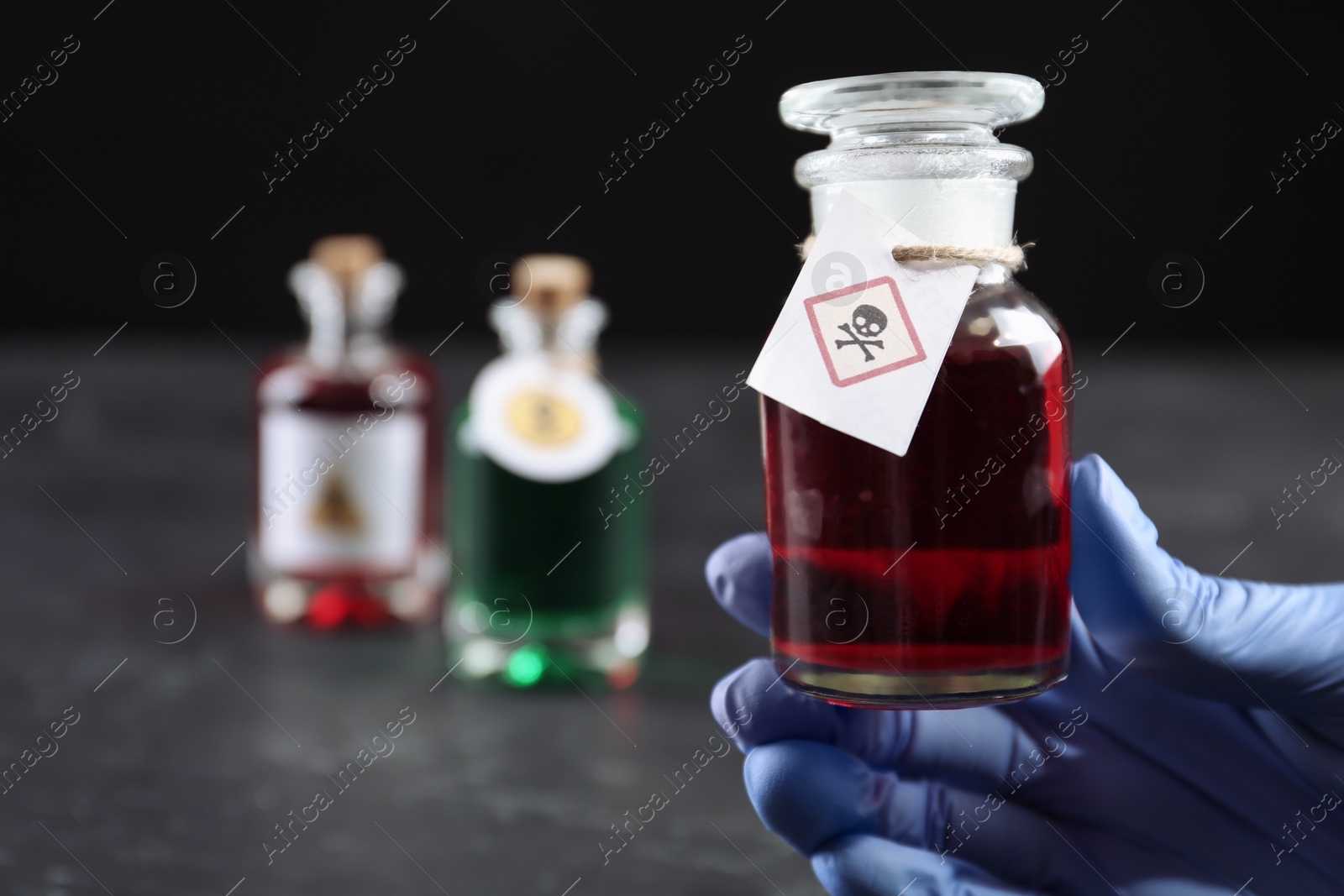 Photo of Woman in gloves holding glass bottle of poison with warning sign over table, closeup. Space for text