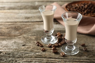 Photo of Coffee cream liqueur in glasses and beans on wooden table, space for text