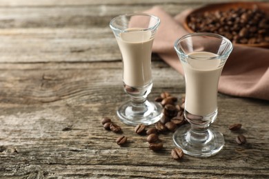 Coffee cream liqueur in glasses and beans on wooden table, space for text