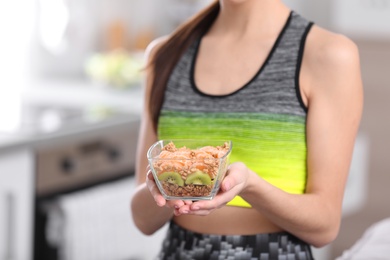 Photo of Young woman in fitness clothes holding bowl of cereal breakfast with fruits at home, closeup