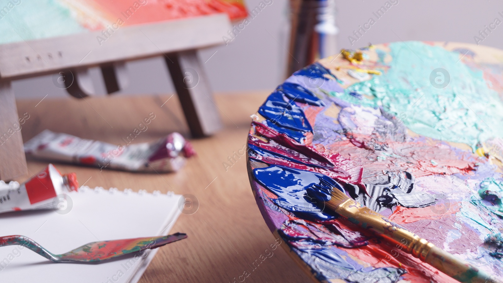 Photo of Applying paint with brush on artist's palette at wooden table, closeup