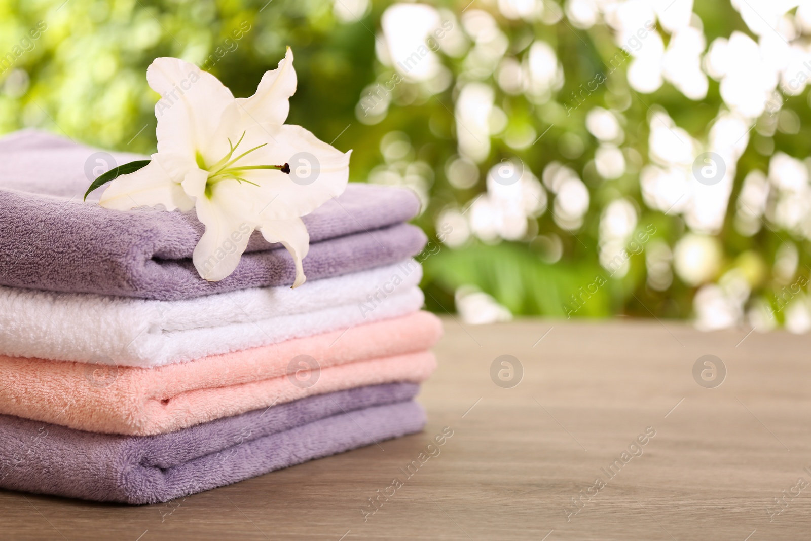 Photo of Stack of clean towels with lily on table against blurred background. Space for text