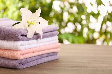 Photo of Stack of clean towels with lily on table against blurred background. Space for text