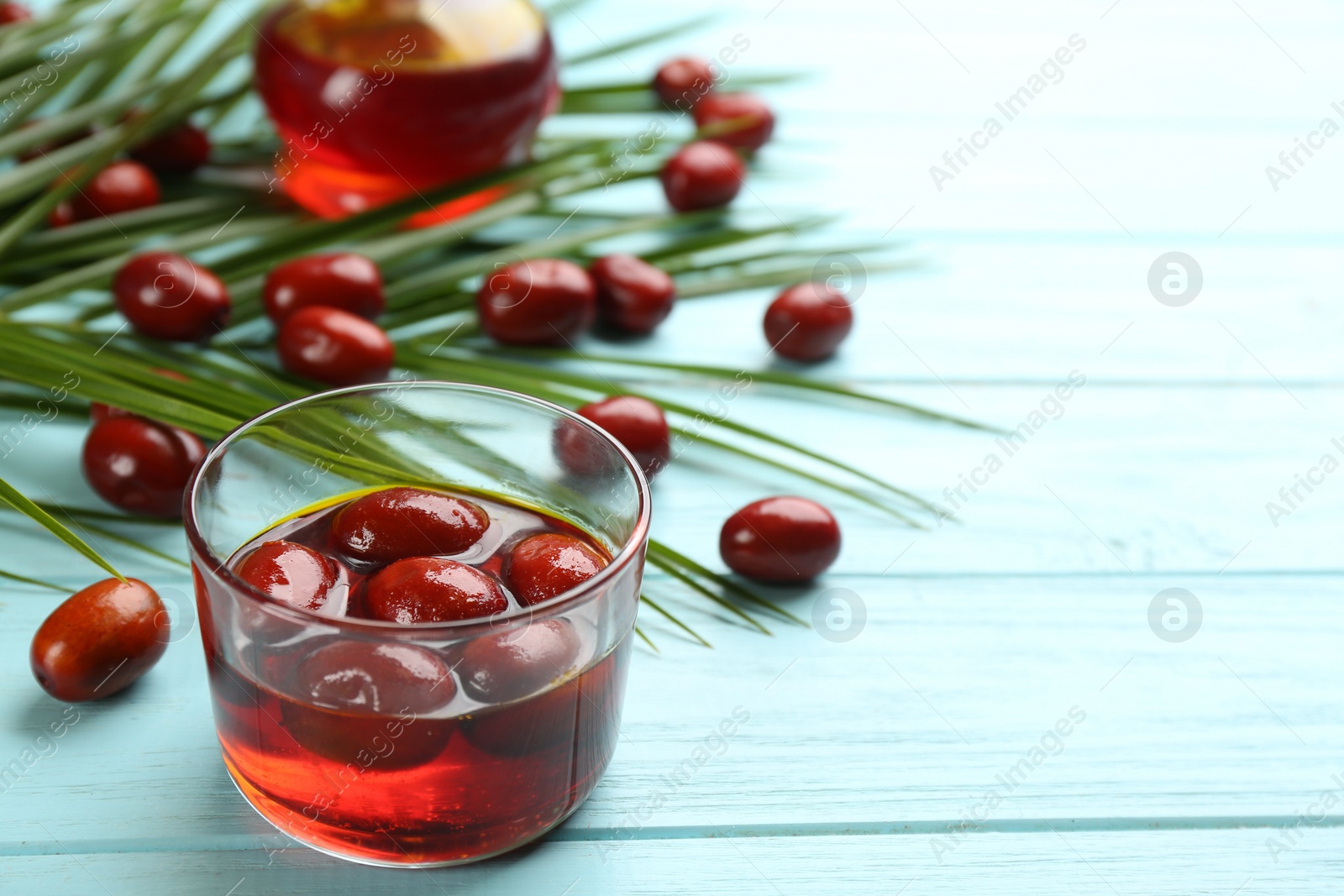 Photo of Palm oil in glass, tropical leaves and fruits on light blue wooden table. Space for text