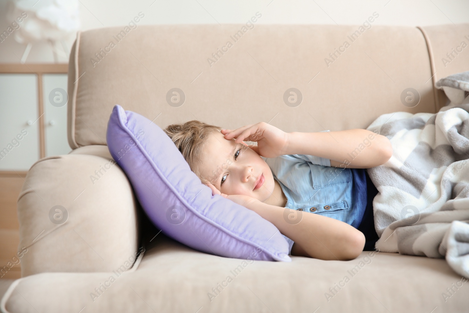 Photo of Little boy suffering from headache while lying on couch at home