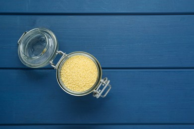 Glass jar of raw couscous on blue wooden table, top view. Space for text