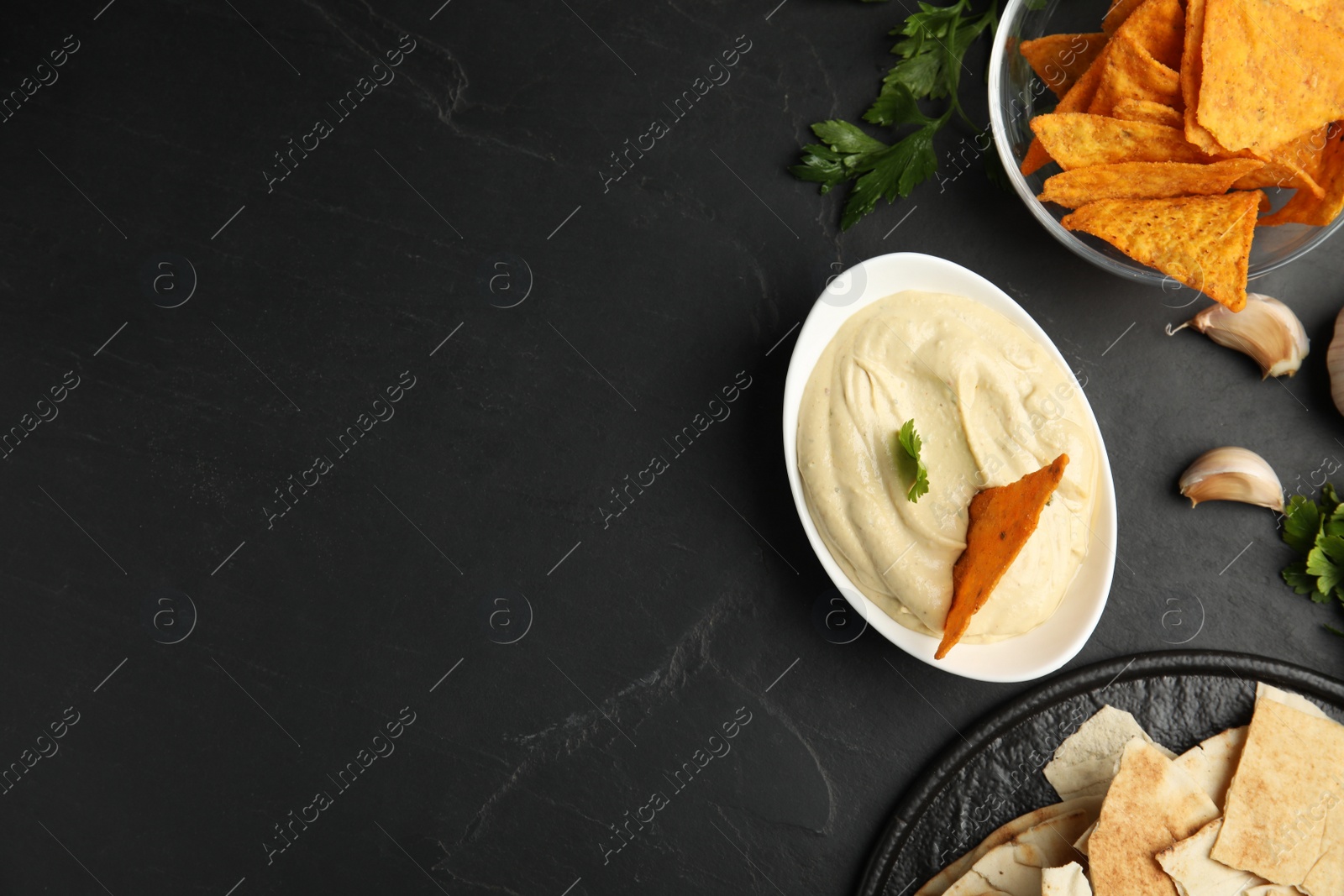 Photo of Delicious hummus with nachos and parsley on black table, flat lay. Space for text