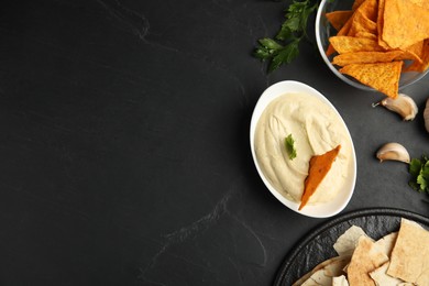 Photo of Delicious hummus with nachos and parsley on black table, flat lay. Space for text