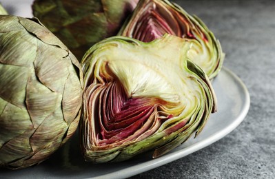 Cut and whole fresh raw artichokes on grey table, closeup