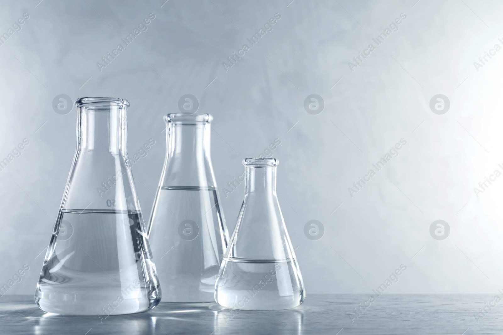Photo of Laboratory glassware with liquid samples for analysis on table against grey background, space for text