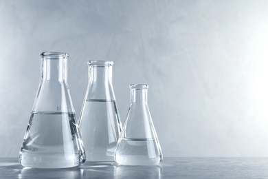 Photo of Laboratory glassware with liquid samples for analysis on table against grey background, space for text