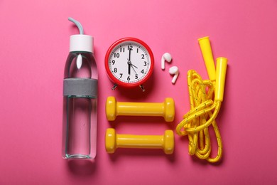 Photo of Bottle of water, alarm clock and sports equipment on pink background, flat lay. Morning exercise