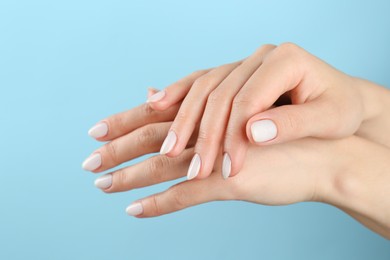 Photo of Woman with white polish on nails against light blue background, closeup