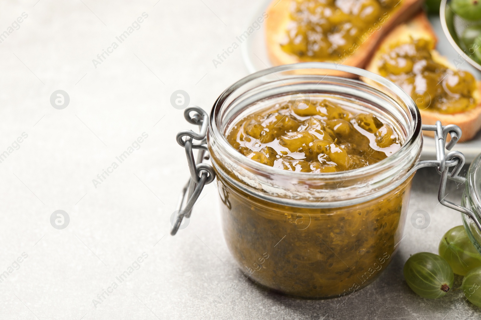 Photo of Jar with delicious gooseberry jam and fresh berries on light grey table, closeup. Space for text