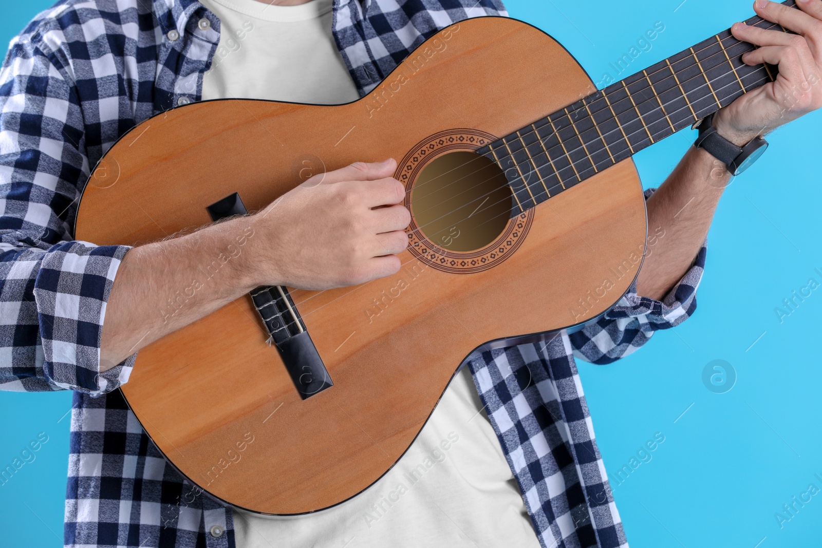 Photo of Young man playing acoustic guitar on color background, closeup