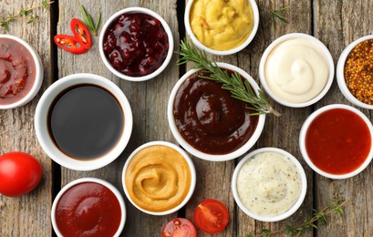 Photo of Different tasty sauces in bowls and ingredients on wooden table, flat lay